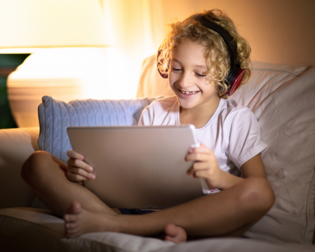 girl with headphones sitting on a couch, smiling with tablet in her hand