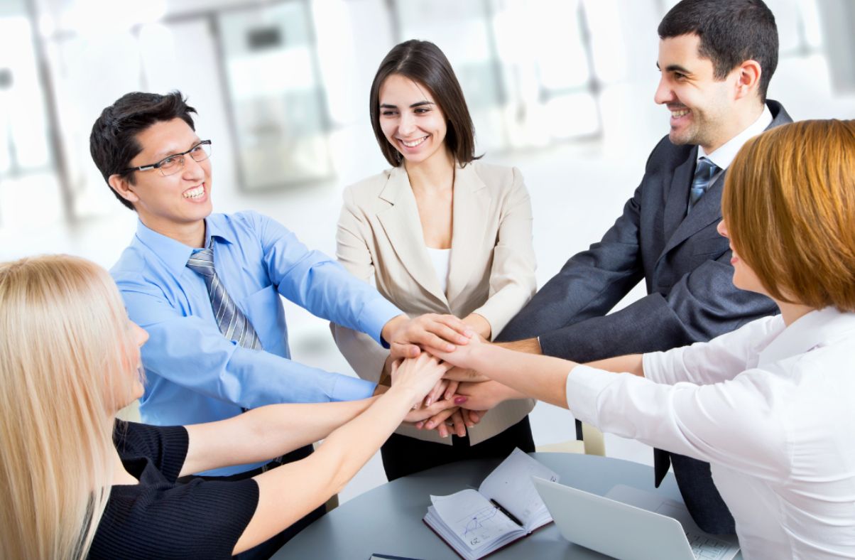 Five colleagues stacking their hands together in a team-building activity at the office.