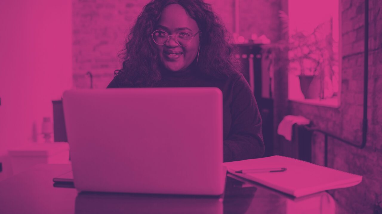 Smiling woman wearing glasses working on a laptop at a desk.