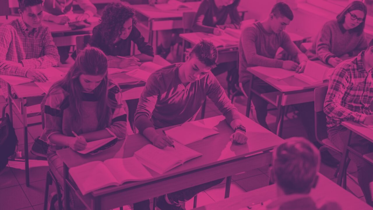Students sitting at desks writing and reading during a classroom session.