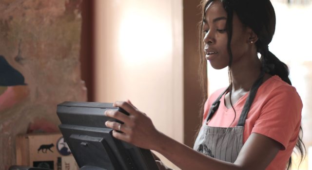 Young retail cashier in apron using a point-of-sale system during onboarding training
